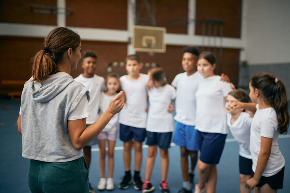 Rear view of physical education teacher talking to her students on a class at school gym.